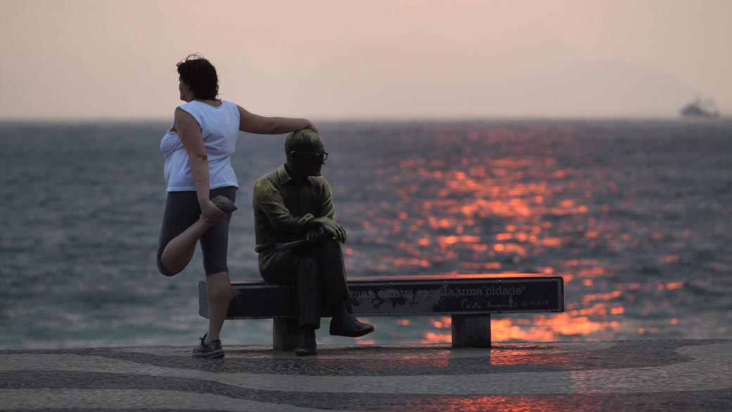 Mulher se apóia na estátua de Carlos Drummond de Andrade durante alongamento em Copacabana, Rio de Janeiro