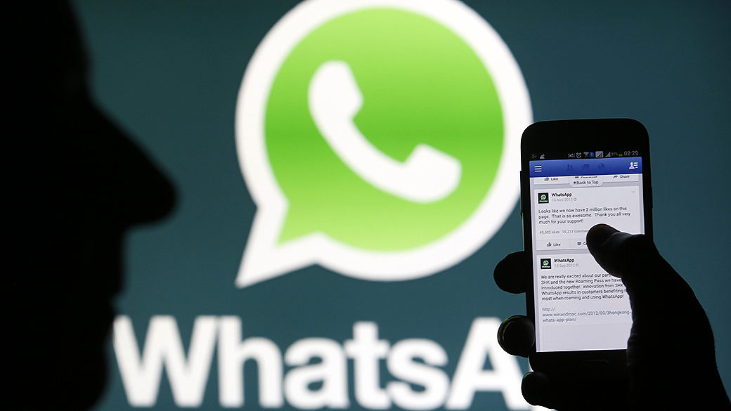 Logo do Whatsapp visto no fundo de um painel enquanto um homem acessa o Facebook através de um smartphone