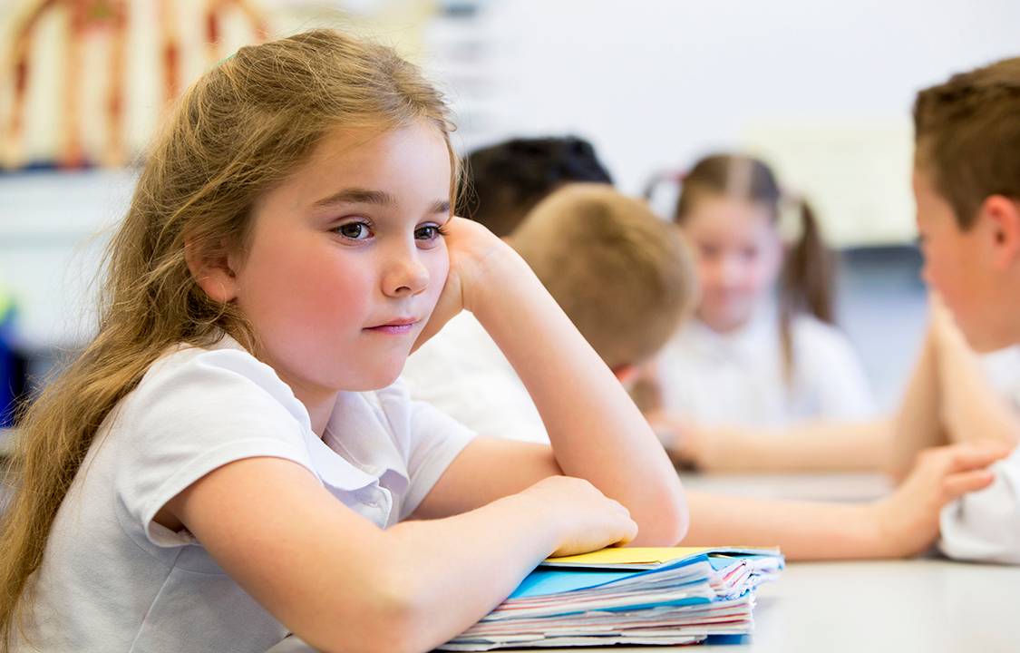A close up shot of a little girl at school who looks distant and upset.