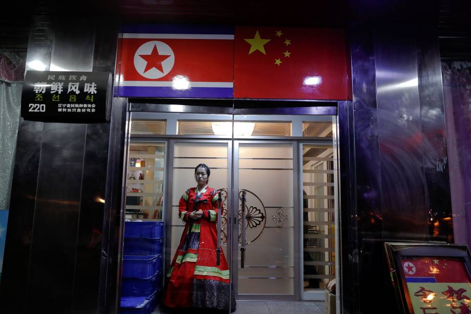 Mulher com vestimentas tradicionais convida pessoas a entrar em um restaurante de comida norte-coreana na cidade de Dandong, China - 30/03/2017