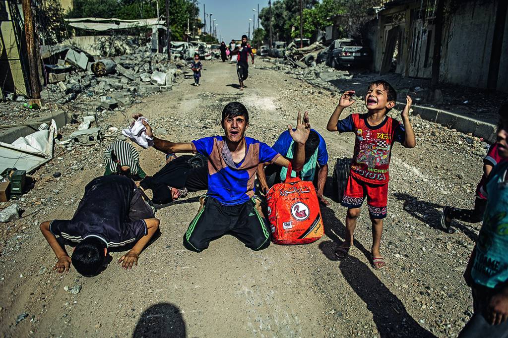 ALÍVIO – Ao deixarem a cidade de Mossul, civis ajoelham-se e erguem as mãos para o céu: sinal de que são inocentes