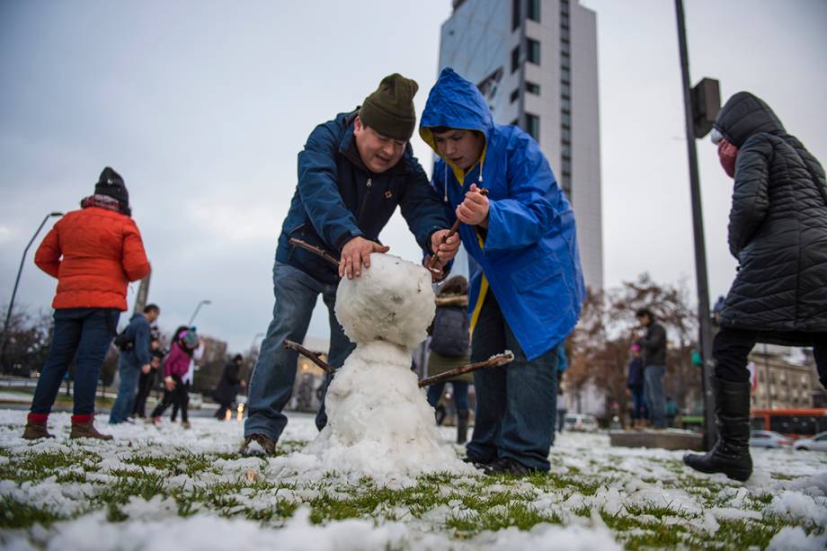 Pai e filho constróem boneco de neve em uma praça no centro de Santiago, após forte nevasca atingir a região, no Chile - 15/07/2017