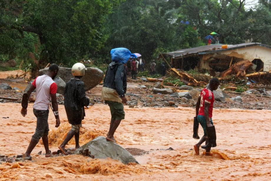 Moradores atravessam uma rua inundada em frente a uma casa em destruída pelas enchentes em Freetown, capital de Serra Leoa - 14/08/2017