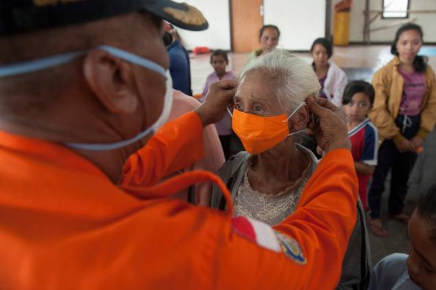 Oficial da agência de gerenciamento de desastres BPBD coloca uma máscara em uma mulher idosa em um abrigo para residentes que tiveram que deixar suas casas devido à erupção do vulcão Monte Agung em Bali, na Indonésia - 27/11/2017 Oficial da agência de gerenciamento de desastres BPBD coloca uma máscara em uma mulher idosa em um abrigo para residentes que tiveram que deixar suas casas devido à erupção do vulcão Monte Agung em Bali, na Indonésia - 27/11/2017