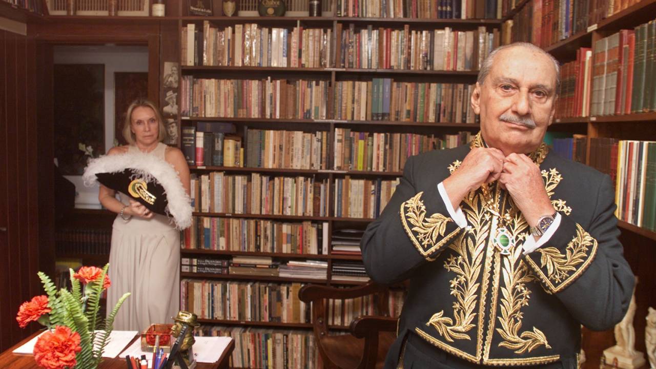 O escritor Carlos Heitor Cony veste o fardão de membro da Academia Brasileira de Letras. Ao fundo, sua mulher Bia segura o chapéu - 30/05/2000
