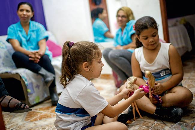 Aprendendo a sobreviver – Momentos de paz no cotidiano de violência na Rocinha: minutos depois de ouvirem tiros a distância e se jogarem no chão, as amigas Yasmin (acima, à esq.), de 6 anos, e Amanda, de 7, brincam tranquilamente de boneca; Camila não larga o filho Davi (abaixo), de 7 meses, que ainda chora muito cada vez que ouve o fogo cruzado