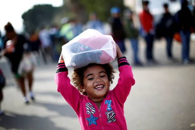 Menina hondurenha, parte da caravana de milhares de pessoas que viajam a caminho dos Estados Unidos, sorri enquanto carrega roupas doadas em um abrigo da cidade mexicana de Tijuana - 21/11/2018 Menina hondurenha, parte da caravana de milhares de pessoas que viajam a caminho dos Estados Unidos, sorri enquanto carrega roupas doadas em um abrigo da cidade mexicana de Tijuana - 21/11/2018