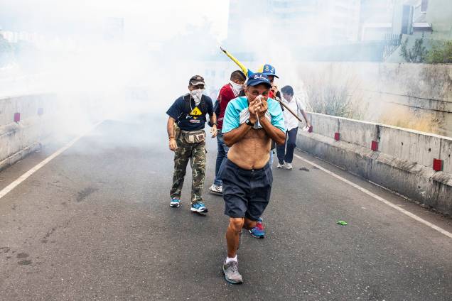 Manifestantes se protegem de bombas de gás lacrimogêneo lançadas pela polícia, durante marcha contra o presidente venezuelano Nicolás Maduro - 23/01/2019 Manifestantes se protegem de bombas de gás lacrimogêneo lançadas pela polícia, durante marcha contra o presidente venezuelano Nicolás Maduro - 23/01/2019