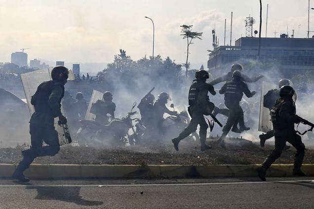 Membros da Guarda Nacional Bolivariana, leais ao presidente Nicolás Maduro, correm sob uma nuvem de gás lacrimogêneo durante confronto com apoiadores de Juan Guaidó em frente à base militar de La Carlota, em Caracas - 30/04/2019 Membros da Guarda Nacional Bolivariana, leais ao presidente Nicolás Maduro, correm sob uma nuvem de gás lacrimogêneo durante confronto com apoiadores de Juan Guaidó em frente à base militar de La Carlota, em Caracas - 30/04/2019