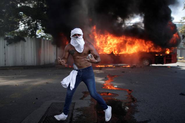 Manifestante de oposição é visto com pedras na frente de ônibus incendiado, próximo da base aérea Generalisimo Francisco de Miranda "La Carlota"em Caracas, capital da Venezuela - 30/04/2019 Manifestante de oposição é visto com pedras na frente de ônibus incendiado, próximo da base aérea Generalisimo Francisco de Miranda "La Carlota"em Caracas, capital da Venezuela - 30/04/2019