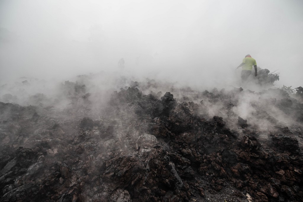 DRCONGO-VOLCANO Residents walk through the smoke from smouldering lava flewing from Mount Nyiragongo in Goma on May 23, 2021. - A river of boiling lava came to a halt on the outskirts of Goma Sunday, sparing the city in eastern DR Congo from disaster after the nighttime eruption of Mount Nyiragongo sent thousands of terrified residents fleeing in panic.