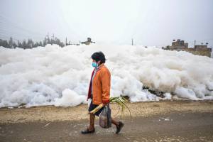 A woman walks by a wall of pungent foam which formed in a polluted river and invaded the Los Puentes neighbourhood, in Mosquera, west of Bogota, on April 26, 2022. (Photo by Juan BARRETO / AFP)