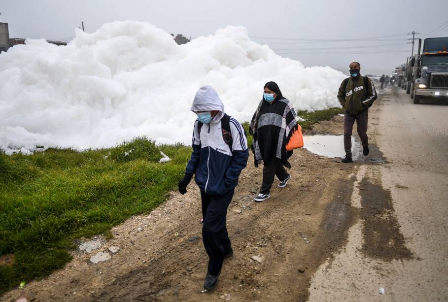 Pessoas caminham pela espuma pungente que se formou em um rio poluído e invadiu o bairro de Los Puentes, em Mosquera, a oeste de Bogotá, em 26 de abril de 2022