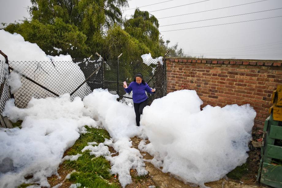 Mulher caminha sobre espuma pungente que se formou em um rio poluído e invadiu o bairro de Los Puentes, em Mosquera, a oeste de Bogotá, em 26 de abril de 2022.