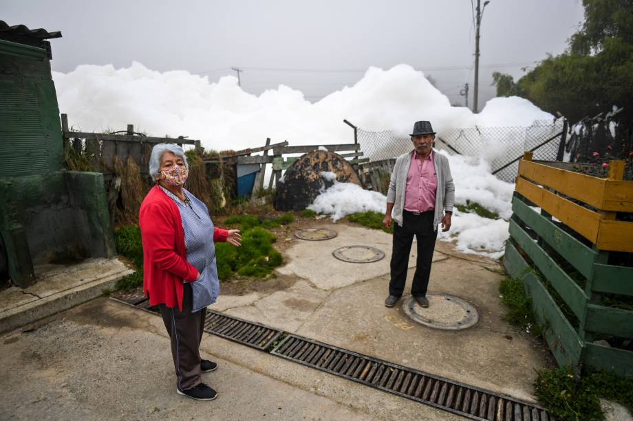 Um homem e uma mulher estão perto de uma espuma pungente que se formou em um rio poluído e invadiu o bairro de Los Puentes, em Mosquera, a oeste de Bogotá, em 26 de abril de 2022.