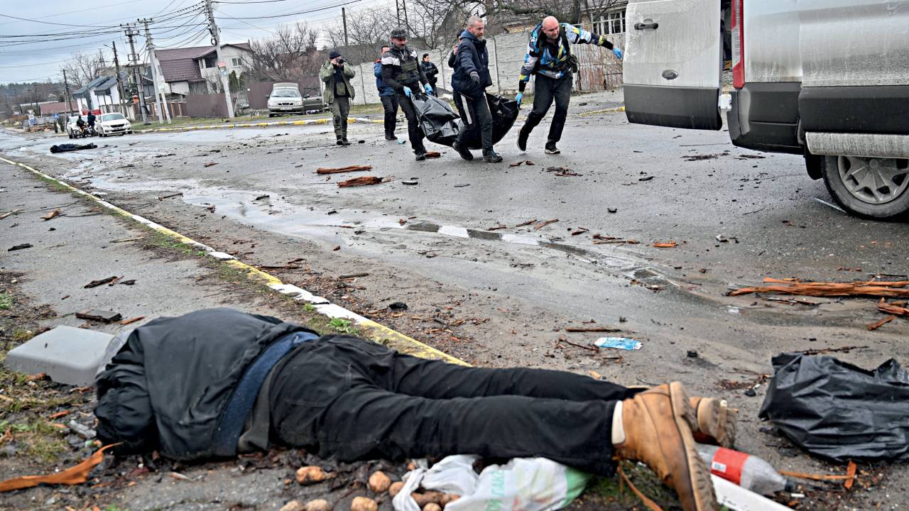 EDITORS NOTE: Graphic content / CAPTION ADDITION - Communal workers carry a civilian in a body bag as another corpse is seen on the ground in the town of Bucha, not far from the Ukrainian capital of Kyiv on April 3, 2022. US and NATO leaders voiced shock and horror at new evidence of atrocities against civilians in Ukraine, and warned that Russian troop movements away from Kyiv did not signal a withdrawal or end to the violence. - The Kremlin on April 4, 2022 rejected accusations that Russian forces were responsible for killing civilians near Kyiv. "We categorically reject all allegations," Kremlin spokesman Dmitry Peskov told journalists. (Photo by Sergei SUPINSKY / AFP)