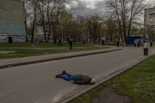 Pessoas olham para o corpo de um civil morto deitado em uma estrada na área residencial que foi atingida pelo bombardeio da artilharia russa, em Kharkiv, nordeste da Ucrânia, 19 de abril de 2022 - Pessoas olham para o corpo de um civil morto deitado em uma estrada na área residencial que foi atingida pelo bombardeio da artilharia russa, em Kharkiv, nordeste da Ucrânia, 19 de abril de 2022 -