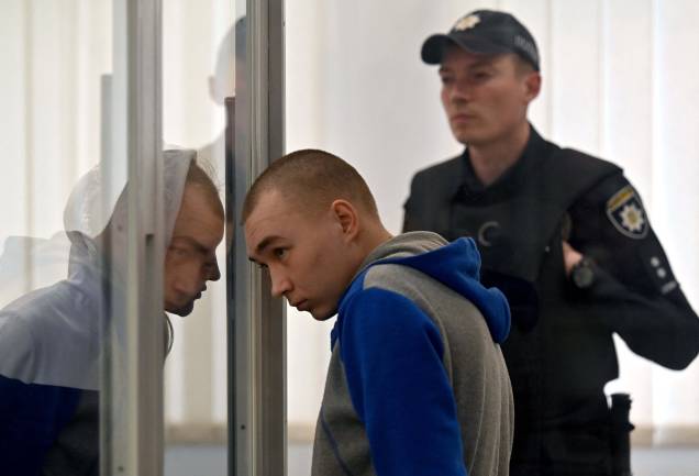 O sargento russo Vadim Shishimarin, ouve a sentença judicial na caixa do réu, no último dia de seu julgamento por acusações de crimes de guerra por ter matado um civil na invasão russa na Ucrânia, em 23/05/2022. O sargento russo Vadim Shishimarin, ouve a sentença judicial na caixa do réu, no último dia de seu julgamento por acusações de crimes de guerra por ter matado um civil na invasão russa na Ucrânia, em 23/05/2022.