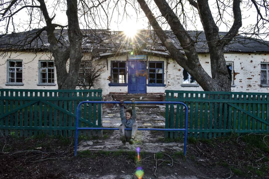 Menino brinca em frente a uma escola na vila de Lukashivka, região de Chernihiv, 27 de abril de 2022. Em 24 de fevereiro, tropas russas entraram no território ucraniano no que o presidente russo declarou uma 'operação militar especial', resultando em combates e destruição no país, um enorme fluxo de refugiados e múltiplas sanções contra a Rússia.