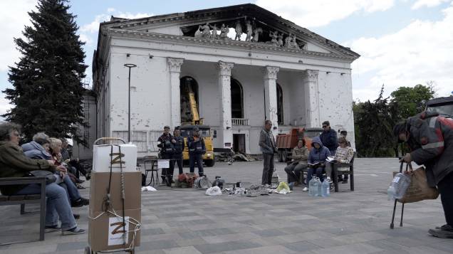 Moradores carregam seus celulares com um gerador, enquanto funcionários de emergências russas, limpa os destroços no teatro de drama Mariupol, parcialmente destruído na cidade de Mariupol em 10 de maio de 2022, em meio à ação militar russa em andamento na Ucrânia. Moradores carregam seus celulares com um gerador, enquanto funcionários de emergências russas, limpa os destroços no teatro de drama Mariupol, parcialmente destruído na cidade de Mariupol em 10 de maio de 2022, em meio à ação militar russa em andamento na Ucrânia.