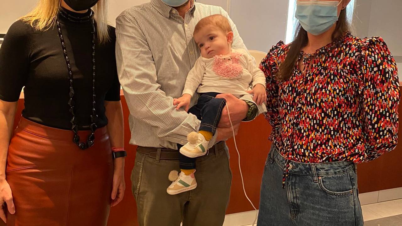 Bebe é segurado por um homem ao lado de duas mulheres