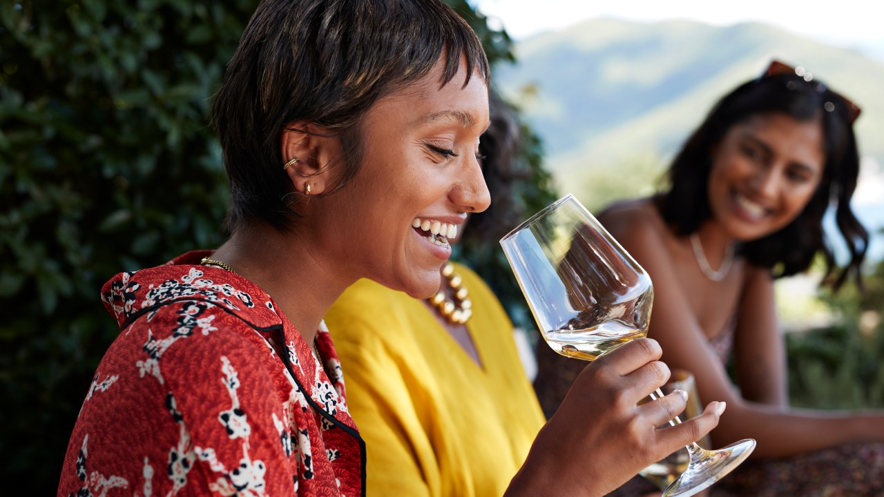 Happy young woman with short hair having white wine by friends