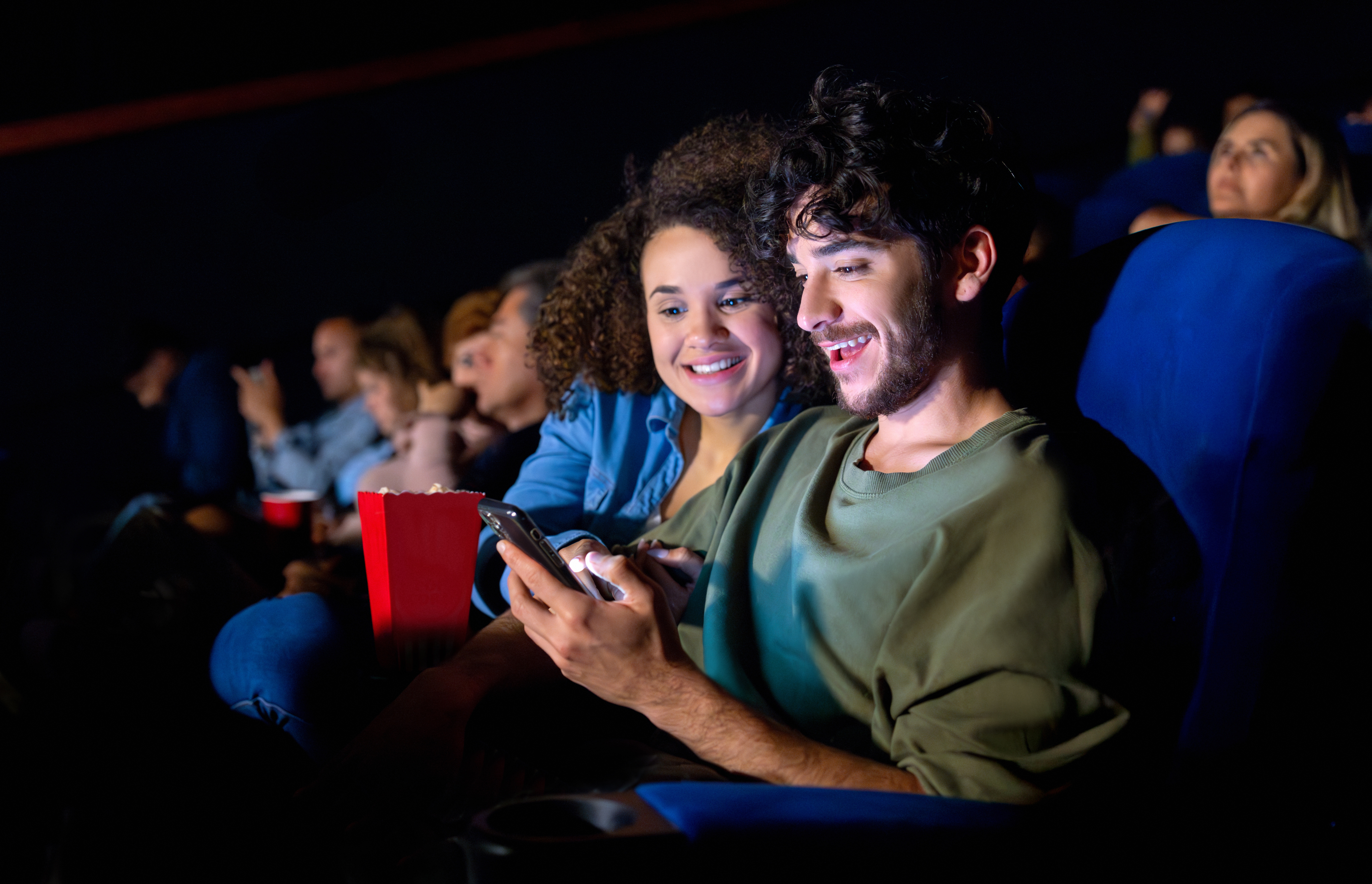 Casal jovem usa celular durante sessão de cinema