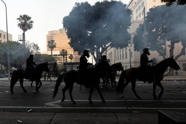 US-POLITICS-IMMIGRATION Los Angeles mounted police advance on a makeshift barricade in a cloud of tear gas as clashes erupt with demonstrators next to City Hall during a protest following federal immigration operations, in Los Angeles, California on June 8, 2025. Demonstrators torched cars and scuffled with security forces in Los Angeles on June 8, as police kept protestors away from the National Guard troops President Donald Trump sent to the streets of the second biggest US city. (Photo by ETIENNE LAURENT / AFP)