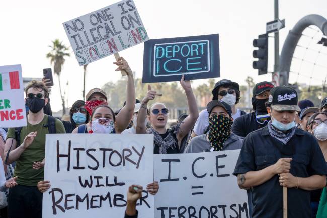 US-POLITICS-IMMIGRATION EDITORS NOTE: Graphic content / People hold placards as protesters clash with law enforcement in the streets surrounding the federal building during a protest following federal immigration operations in Los Angeles, California, on June 8, 2025. Demonstrators torched cars and scuffled with security forces in Los Angeles on June 8, as police kept protestors away from the National Guard troops President Donald Trump sent to the streets of the second biggest US city. (Photo by RINGO CHIU / AFP)