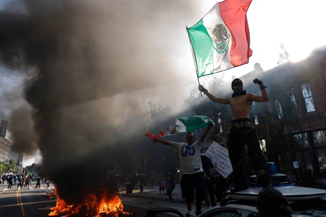 Protests Erupt In L.A. County, Sparked By Federal Immigration Raids LOS ANGELES, CALIFORNIA - JUNE 08: Protesters hold Mexican flags while standing on a Waymo car during a protest against immigration raids on June 08, 2025 in Los Angeles, California. Tensions in the city remain high after the Trump administration called in the National Guard against the wishes of city leaders following two days of clashes with police during a series of immigration raids. More protests are scheduled for today. Mario Tama/Getty Images/AFP (Photo by MARIO TAMA / GETTY IMAGES NORTH AMERICA / Getty Images via AFP)