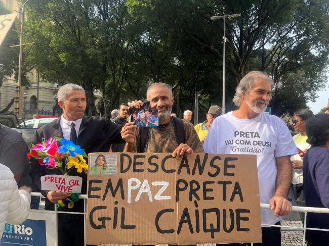Fã Preta Fã de Preta Gil com cartaz e uma foto ao lado da cantora aguardando o velório no Theatro Municipal