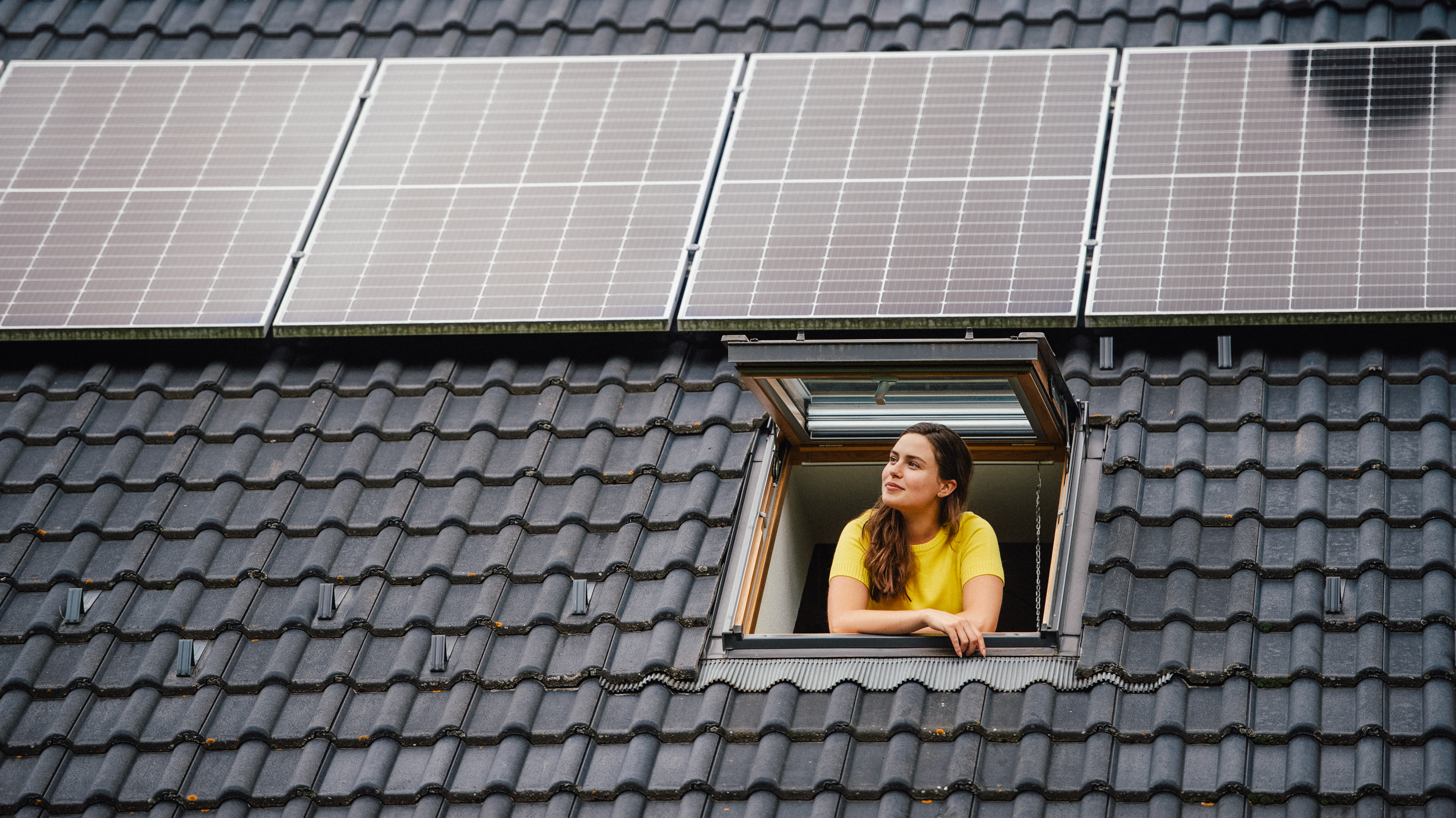 Beautiful woman looking out of a skylight with a rooftop solar panel system above her.
