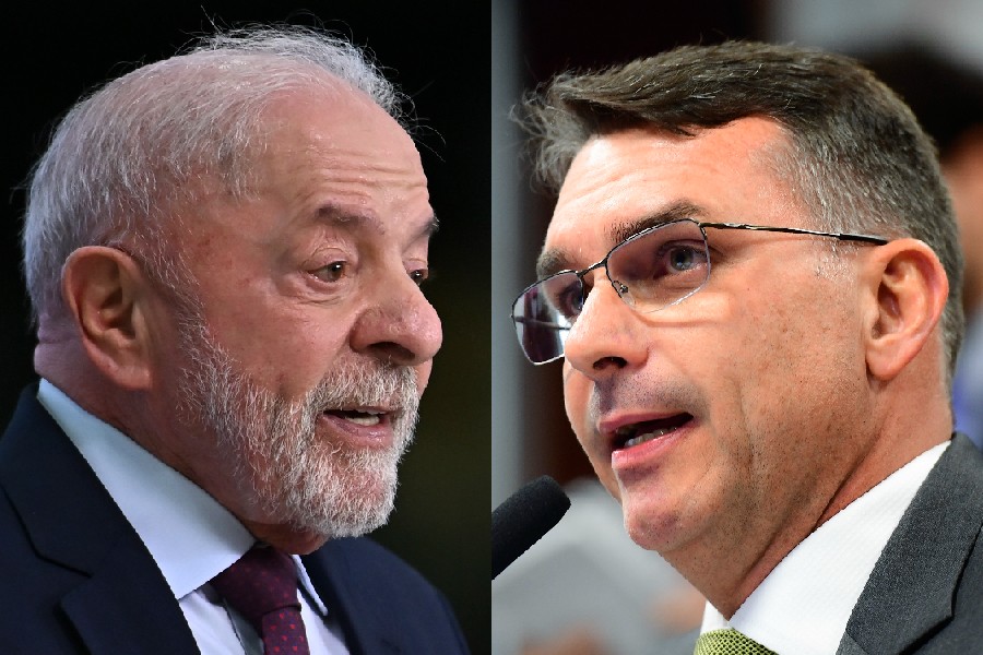 Lula, com barba e cabelo grisalhos, terno azul-marinho e gravata vinho, à esquerda, e um homem de óculos, terno cinza e gravata verde-limão, à direita, ambos com a boca aberta, falando em microfones invisíveis